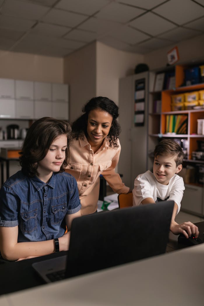 Teacher assisting diverse students in a classroom with a laptop, promoting teamwork and education.